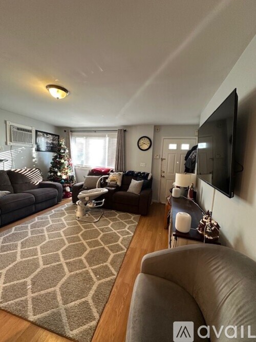 A living room with a Christmas tree and a flat screen TV mounted on the wall.