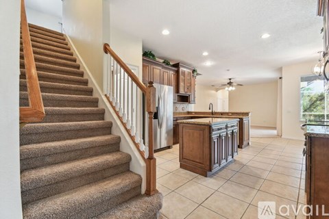 A spacious kitchen with wooden cabinets and a staircase with a carpeted runner.