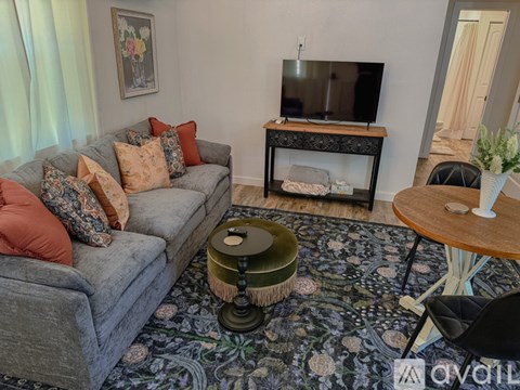 A grey couch with red pillows sits in front of a television in a living room.