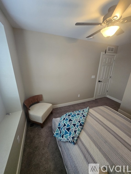 A bedroom with a bed, chair, and ceiling fan.