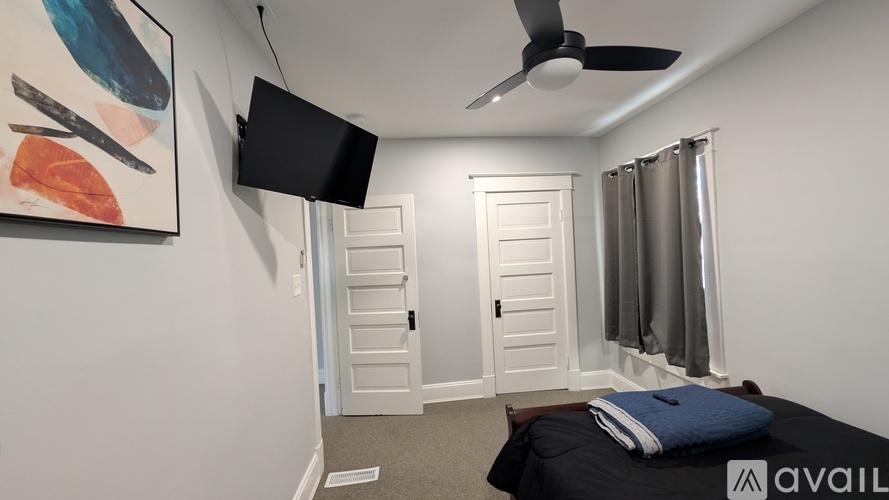 A room with a bed, a painting, a fan, and a window with curtains.