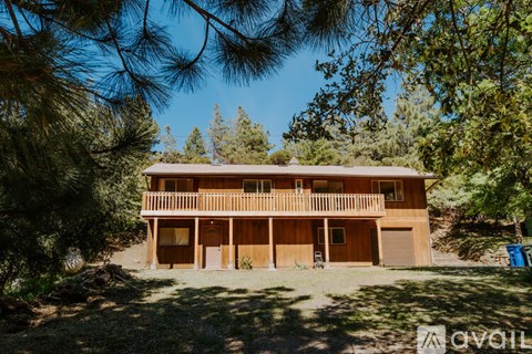 A wooden house with a porch is surrounded by trees.