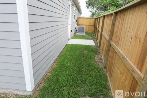 A narrow strip of grass separates a grey house from a wooden fence.
