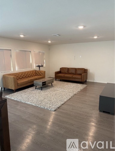 A living room with a brown sofa, a white rug, and a wooden floor.