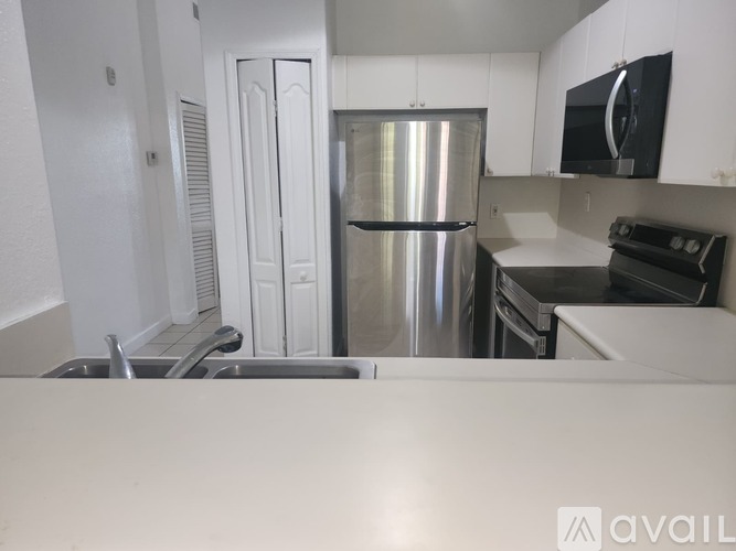 A kitchen with a stainless steel refrigerator, black microwave, and white cabinets.