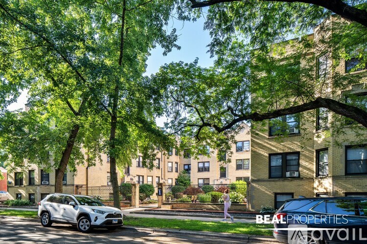 A white car is parked on a street lined with trees and apartment buildings.