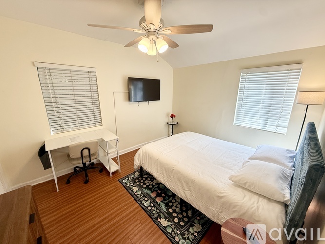A bedroom with a bed, desk, and television.