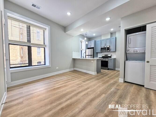 A spacious room with light wood flooring and a kitchen area with white appliances.