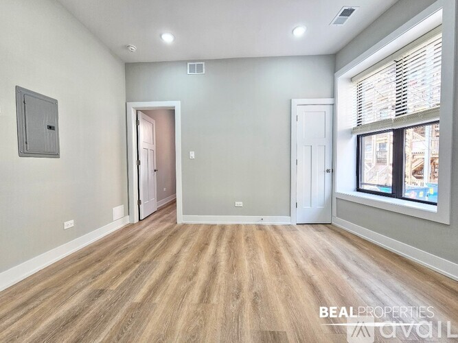 A spacious room with wooden flooring and a window with blinds.