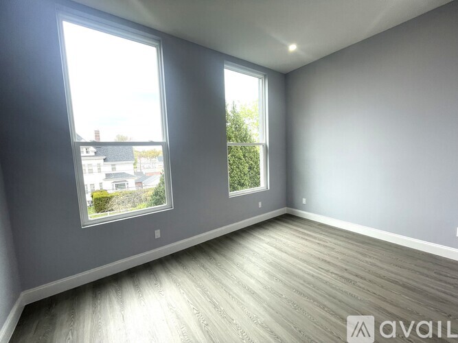 A room with two windows and wooden flooring is available for rent.