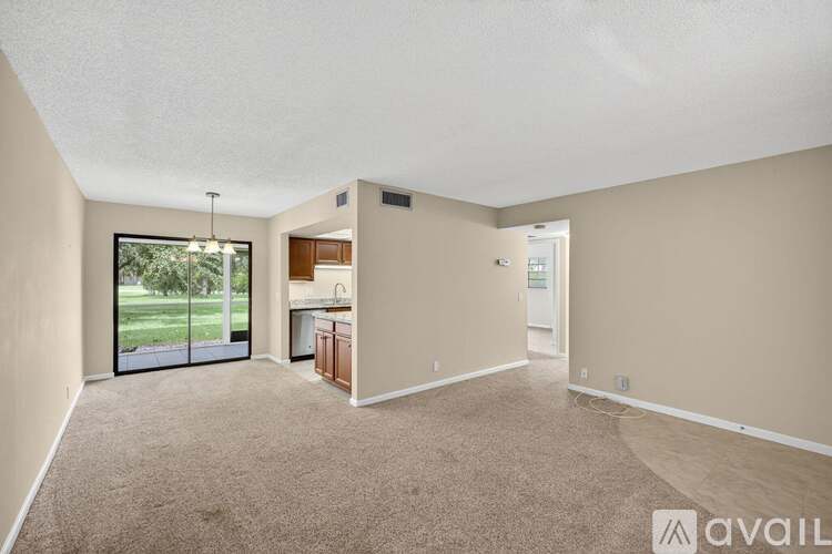 A spacious room with beige carpeting and a sliding glass door leading to a backyard.