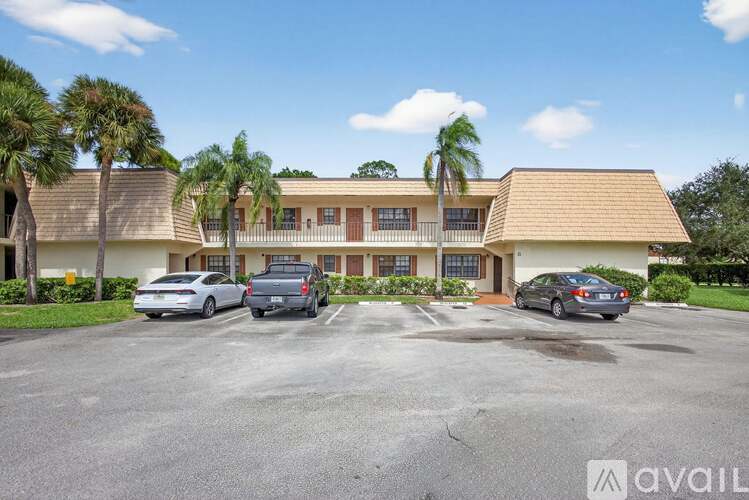 A building with a parking lot in front of it and palm trees around.