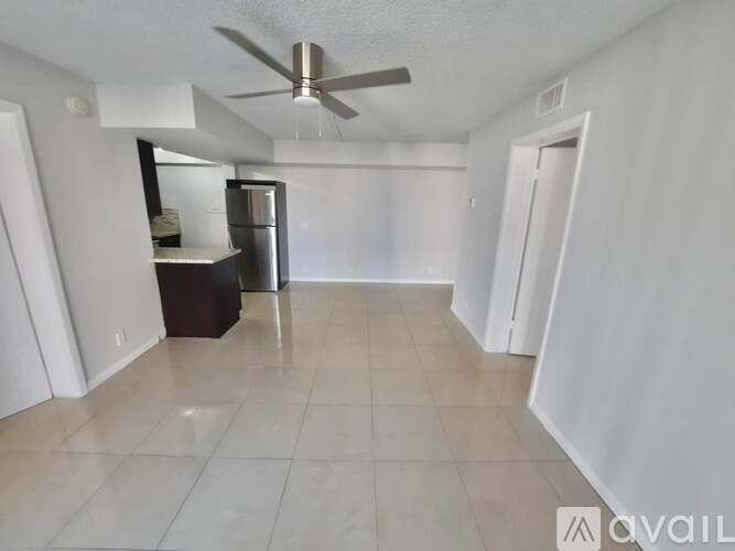 A spacious room with a ceiling fan and a refrigerator.