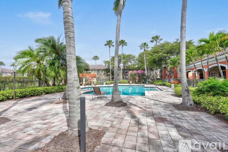 A pool surrounded by palm trees and a brick patio.