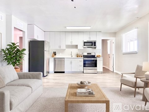 A modern kitchen with white cabinets and appliances, a dining table with chairs, and a living room with a sofa and a coffee table.