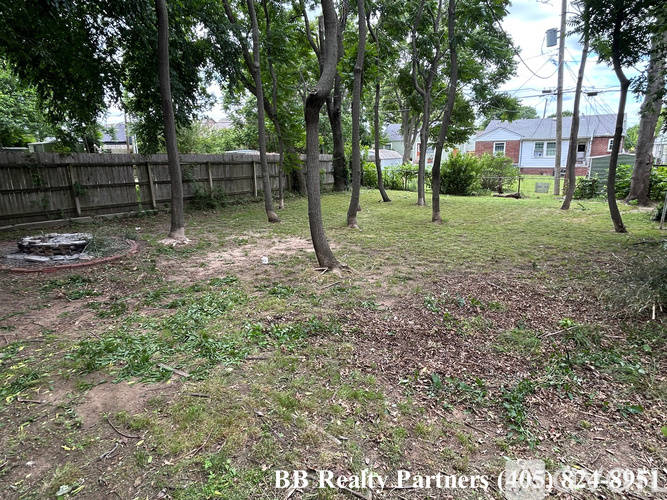A backyard with a dirt area, trees, and a fence.