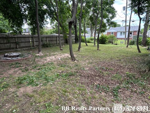 A backyard with a dirt area, trees, and a fence.