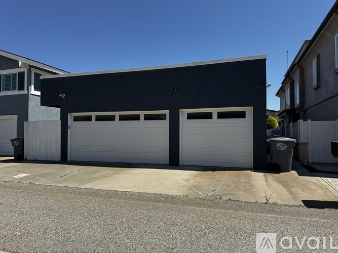 A two-car garage with a black exterior and white doors is situated on a street.