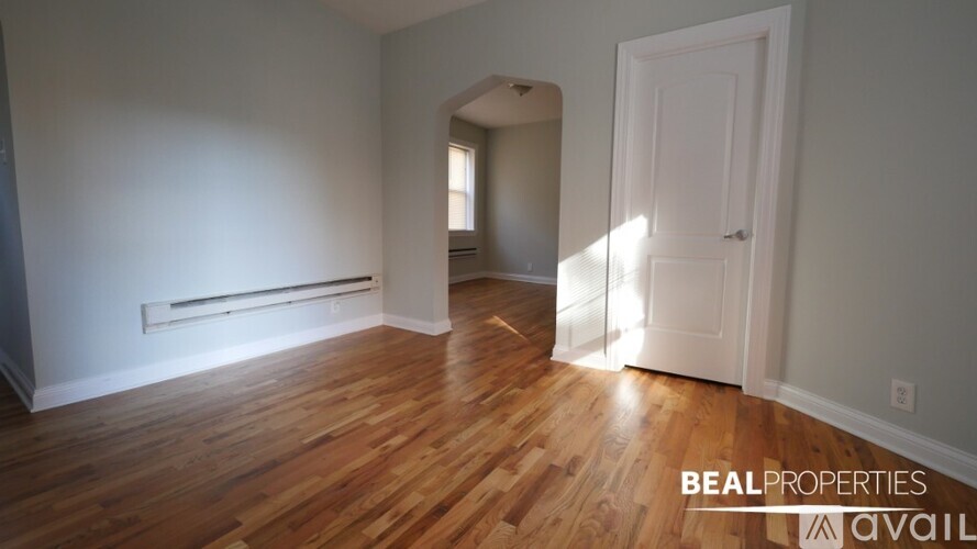 A room with wooden floors and white walls, with a door on the right side.