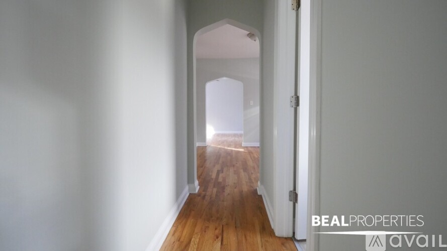 A hallway with a wooden floor and white walls leading to a bright room.