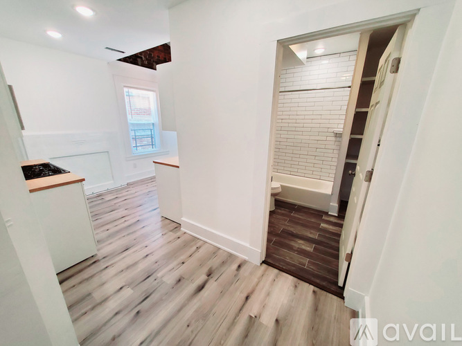 A room with a wooden floor and a white wall with a doorway leading to another room.