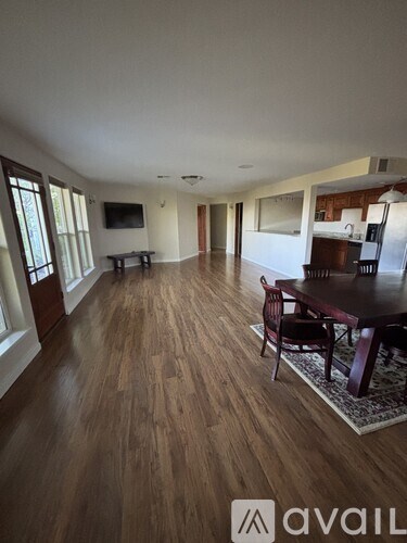 A living room with a wooden floor and a dining table with chairs.