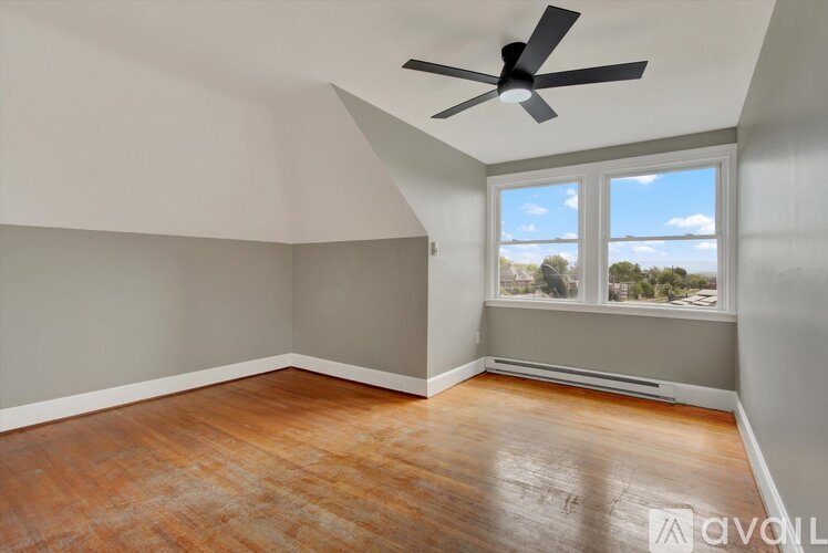 A room with a ceiling fan and a window overlooking a parking lot.