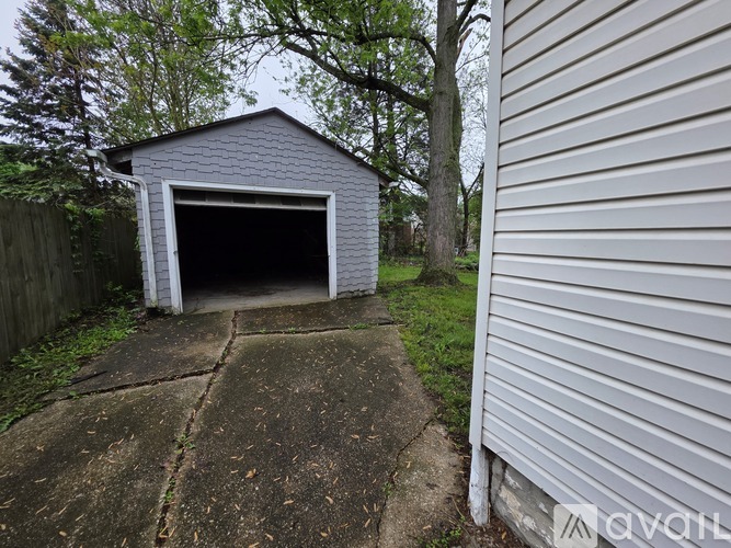 A small garage with a door open is situated next to a house.