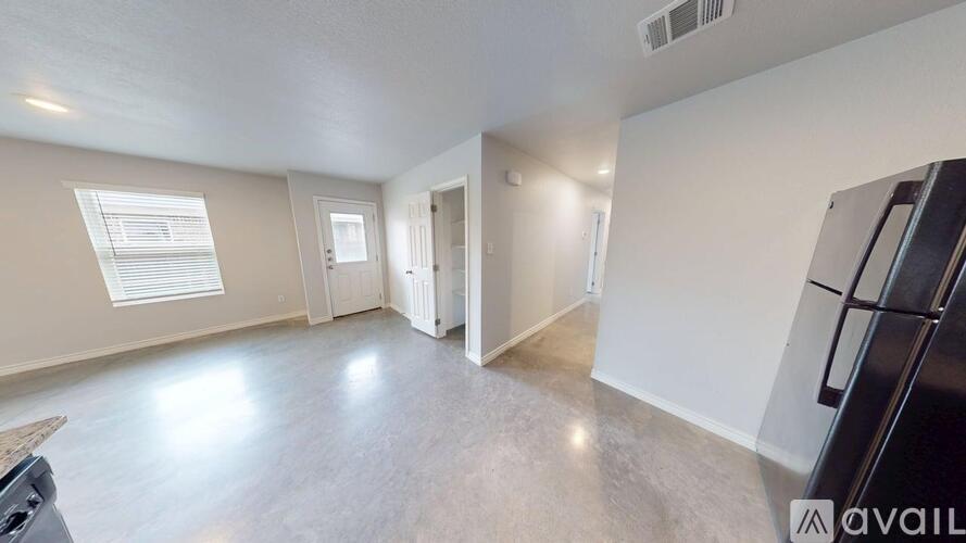 A spacious empty room with a black refrigerator on the right side.