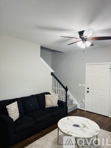A black couch with two pillows sits in a room with a ceiling fan.
