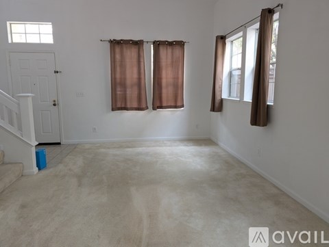 A room with a carpeted floor, a staircase, and two windows with curtains.
