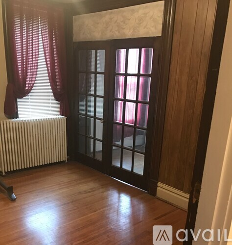 A room with a wooden floor, a window with red curtains, and a closed door.