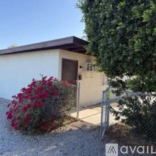 A small house with a brown door and a fence with flowers in front.
