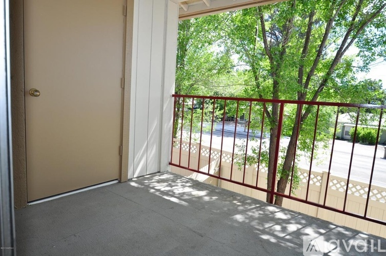 A balcony with a red railing and a view of trees and a street.