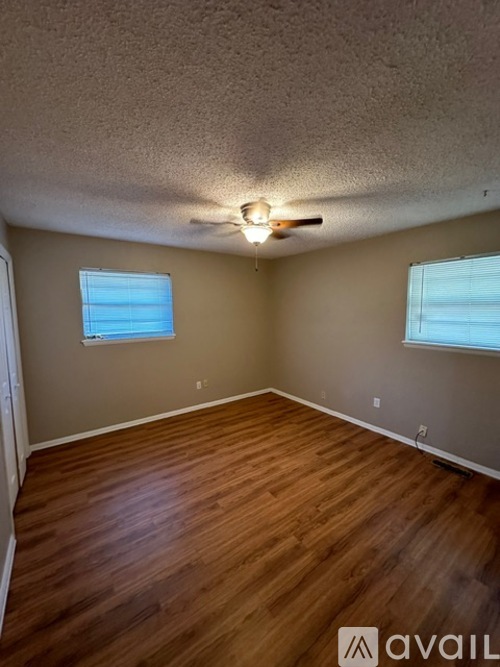 A room with wooden flooring and two windows.