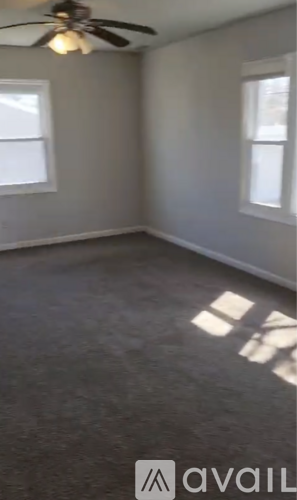 A room with a ceiling fan and two windows.
