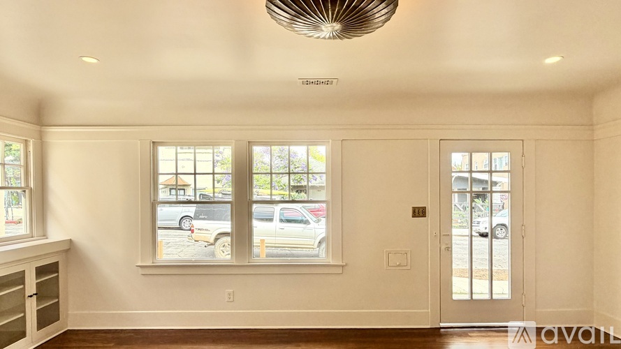 A room with a ceiling fan and a window showing a parking lot outside.