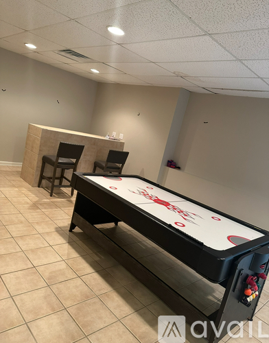 A pool table with a red and white cloth is in the middle of a room with two chairs and a wooden cabinet.