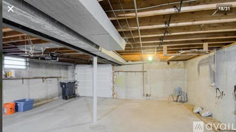 A spacious garage with a concrete floor and walls, equipped with a garage door opener and a workbench.