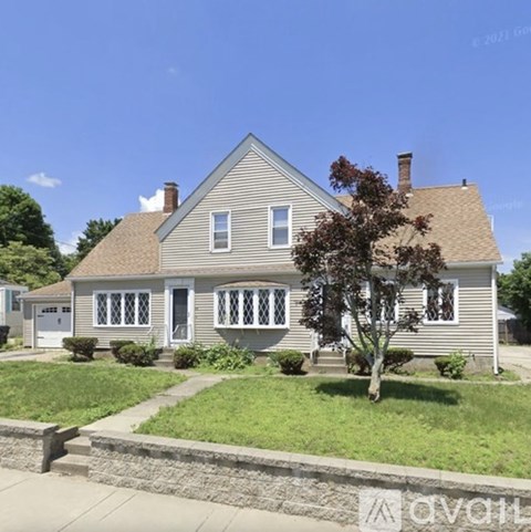A house with a grey roof and white trim is surrounded by a grassy lawn and a sidewalk.