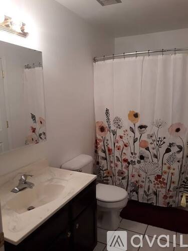 A bathroom with a floral shower curtain and a white sink.