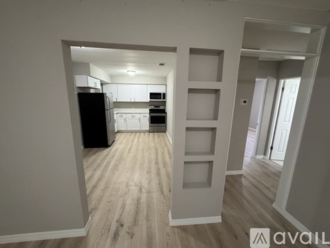 A kitchen with a black refrigerator and white cabinets is visible through a doorway.