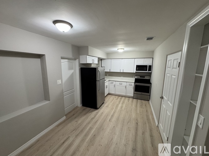 A kitchen with a black refrigerator, white cabinets, and wooden floors.