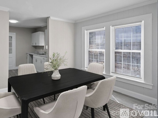 A black dining table with four chairs and a vase of flowers sits in a room with a kitchen in the background.