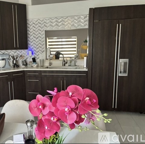 A kitchen with brown cabinets and a white countertop with a vase of pink flowers in the foreground.