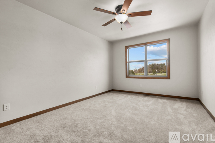 A room with a ceiling fan and a window showing a view of trees and sky.