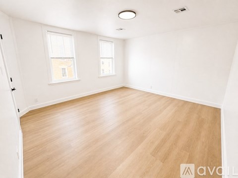 A room with wooden flooring and two windows.