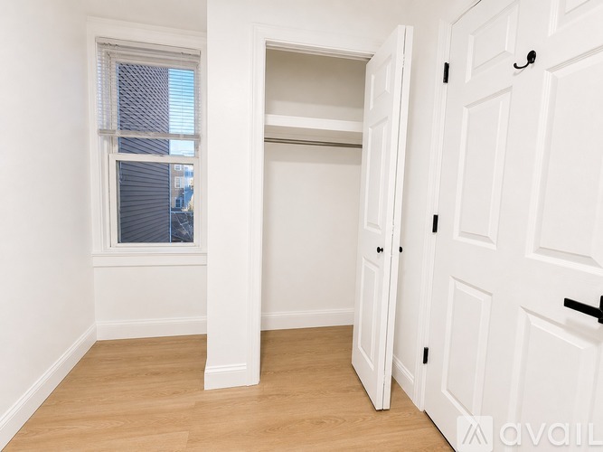 A white door is open to a room with a window and a wooden floor.