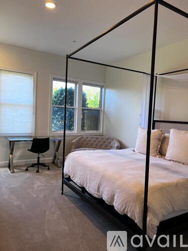 A bedroom with a four poster bed, a desk with a chair, and a window.