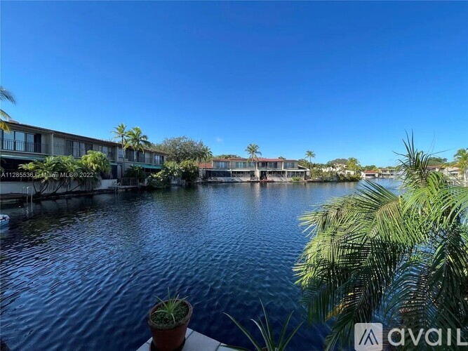 A view of a calm body of water with buildings and palm trees in the background.
